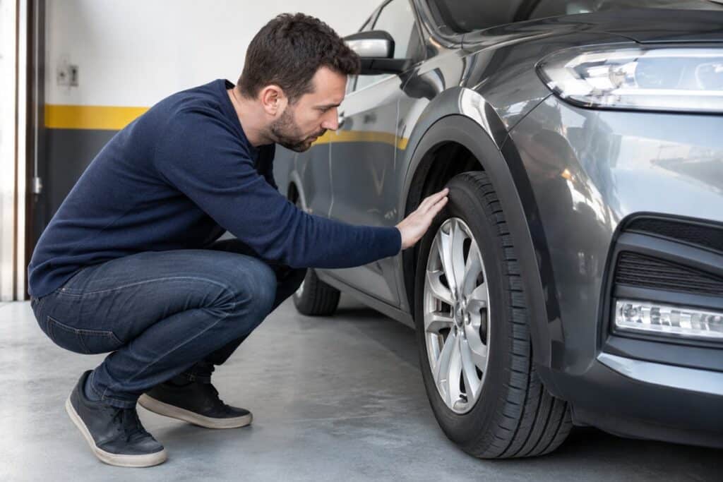 homme qui touche et regarde pneu voiture