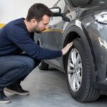 homme qui touche et regarde pneu voiture